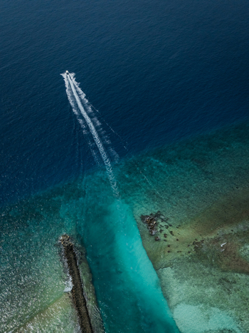 Aerial view of a boat slicing through the turquoise channel into the deep blue sea creating a stark contrast of colors Vashafaru Island Thiladhummathi Atoll Maldives.