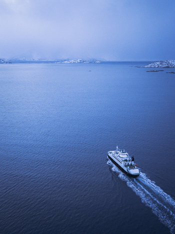 Aerial view of a ferry cutting through the dark blue water leaving a foamy white trail in its wake Sommar&oslash;y Troms Norway.