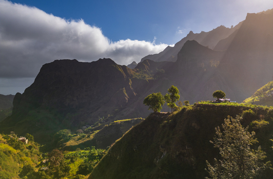 Aerial view of Trilha do Vale do Paul winding through lush green mountains with dramatic sunlight and shadows in Faja de Cima Paul Cabo Verde.