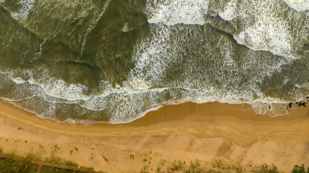 Aerial view of waves crashing onto the sandy beach with green vegetation along the coastline in Devgad Maharashtra India. Aerial view of waves crashing onto the sandy beach with green vegetation along the coastline in Devgad Maharashtra India.