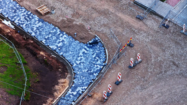 Aerial view of a construction site featuring a newly laid blue grey tiled walkway surrounded by gravel dirt and safety barriers in Latvia. Aerial view of a construction site featuring a newly laid blue grey tiled walkway surrounded by gravel dirt and safety barriers in Latvia.