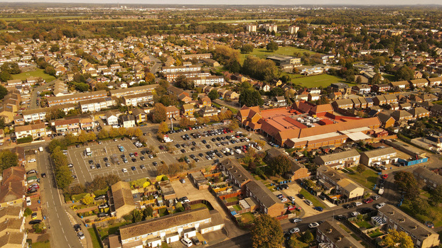 Aerial view of a suburban shopping center with a large parking lot surrounded by residential houses and green spaces in England United Kingdom. Aerial view of a suburban shopping center with a large parking lot surrounded by residential houses and green spaces in England United Kingdom.