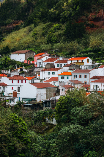 View of a cluster of charming white houses with striking red tiled roofs nestled amidst verdant hills blending rustic charm with nature s embrace Furnas Azores Portugal.