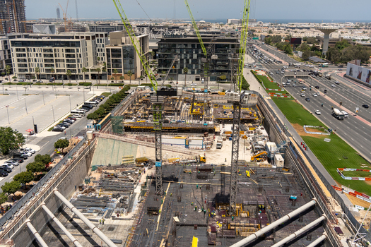 Aerial view of a large urban construction site with green tower cranes and workers near modern buildings and a busy highway in Dubai Dubai United Arab Emirates. Aerial view of a large urban construction site with green tower cranes and workers near modern buildings and a busy highway in Dubai Dubai United Arab Emirates.
