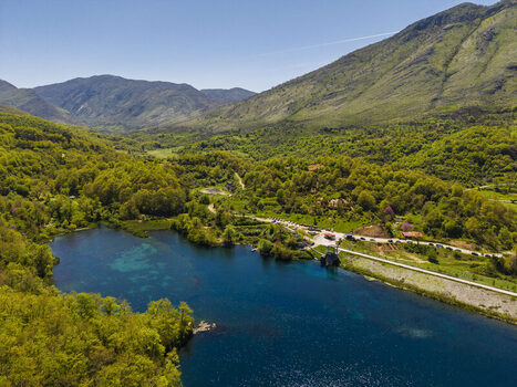 Aerial view of Blue Eye spring surrounded by lush green forests and mountains under a clear blue sky Finiq Vlore County Albania.