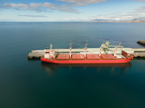 Aerial view of a large red cargo ship docked at the industrial port with cranes and calm blue water under a clear sky in Hafnarfjordur Hafnarfjardarkaupstad Iceland. Aerial view of a large red cargo ship docked at the industrial port with cranes and calm blue water under a clear sky in Hafnarfjordur Hafnarfjardarkaupstad Iceland.