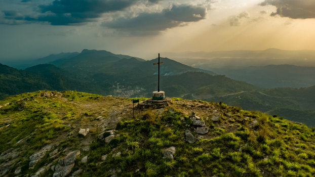 Aerial view of the cross atop Mt. Gemi surrounded by lush green mountain slopes and rocky terrain under a dramatic golden hour sky in Amedzofe Volta Region Ghana. Aerial view of the cross atop Mt. Gemi surrounded by lush green mountain slopes and rocky terrain under a dramatic golden hour sky in Amedzofe Volta Region Ghana.