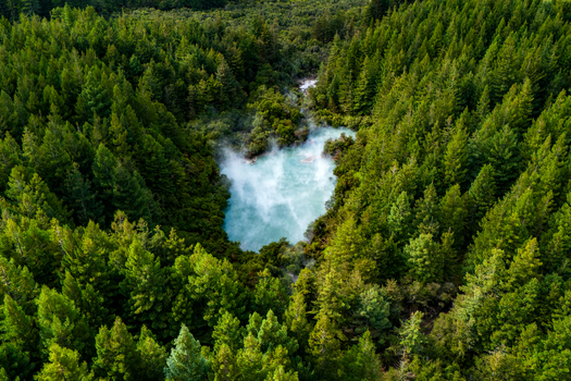 Aerial view of a steaming pool nestled deep within a dense forest where verdant trees meet the ethereal turquoise waters Waiotapu Thermal Wonderland New Zealand. Aerial view of a steaming pool nestled deep within a dense forest where verdant trees meet the ethereal turquoise waters Waiotapu Thermal Wonderland New Zealand.