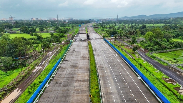 Aerial view of the Delhi Mumbai Expressway under construction surrounded by lush green fields trees and infrastructure in Badlapur Maharashtra India. Aerial view of the Delhi Mumbai Expressway under construction surrounded by lush green fields trees and infrastructure in Badlapur Maharashtra India.