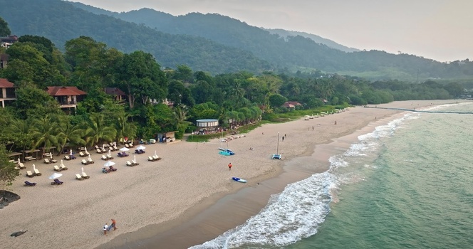 Aerial view of a tropical beach resort featuring palm trees lounge chairs on the sand and turquoise ocean waves in Thailand. Aerial view of a tropical beach resort featuring palm trees lounge chairs on the sand and turquoise ocean waves in Thailand.