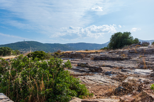 View of the Ancient Theatre of Thorikos archaeological site with rocky ruins and green bushes under a blue sky in Thoricus Greece.