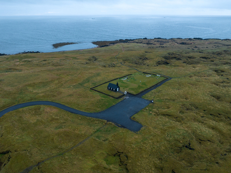 Aerial view of the stark black B&uacute;&eth;akirkja church stands in sharp contrast against the vast green and brown landscape B&uacute;&eth;ir Sn&aelig;fellsb&aelig;r Iceland.