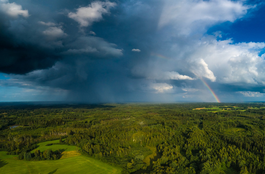Aerial view of a dramatic storm cloud with a rainbow over the lush green forests and fields of Latvia. Aerial view of a dramatic storm cloud with a rainbow over the lush green forests and fields of Latvia.
