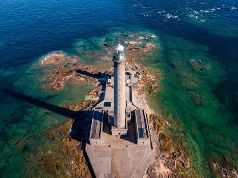Aerial view of Gatteville Lighthouse standing on a rocky outcrop surrounded by clear turquoise waters in Gatteville le Phare Normandie France.