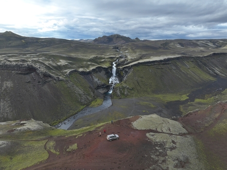 Aerial view of Eldgja volcanic canyon featuring a waterfall cascading down basalt cliffs with a parked car and people in the mossy highlands of Kirkjubaejarklaustur Skaftarhreppur Iceland. Aerial view of Eldgja volcanic canyon featuring a waterfall cascading down basalt cliffs with a parked car and people in the mossy highlands of Kirkjubaejarklaustur Skaftarhreppur Iceland.