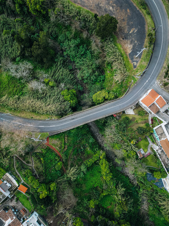 Aerial view of a winding road cutting through lush green foliage and quaint houses a tapestry of nature and civilization blending seamlessly Agua de Alto Azores Portugal.