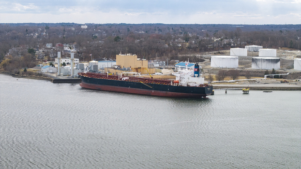 Aerial view of a colossal tanker ship docked near industrial tanks its dark hull a stark contrast to the bright tanks and water Quincy Massachusetts United States.
