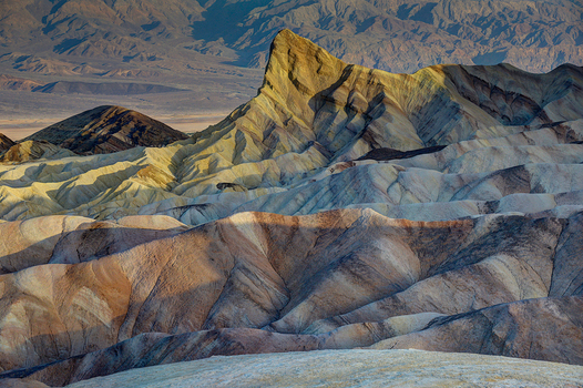 View of the colorful eroded badlands of Death Valley National Park featuring dramatic golden and tan ridges under soft light in Death Valley California United States.