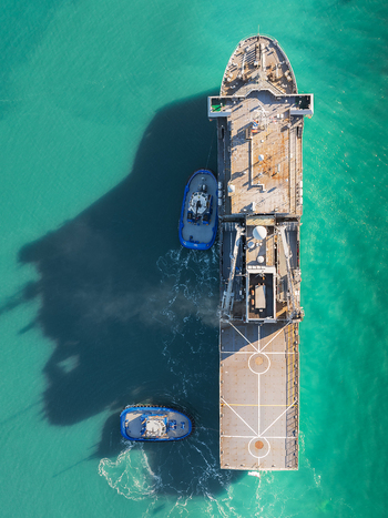 Aerial view of a large ship being assisted by two tugboats in the turquoise waters of Lyttelton Harbour Christchurch Canterbury Region New Zealand.