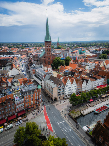 Aerial view of red roofed buildings clustered around the towering spire of St. Mary s Church under a sky streaked with clouds L&uuml;beck Schleswig Holstein Germany.