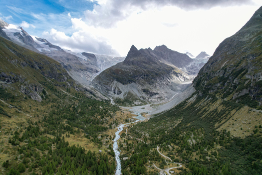 Aerial view of the Ferpecle glacier valley with the winding glacial stream surrounding pine forests and rugged mountain peaks in Evolene Valais Switzerland. Aerial view of the Ferpecle glacier valley with the winding glacial stream surrounding pine forests and rugged mountain peaks in Evolene Valais Switzerland.