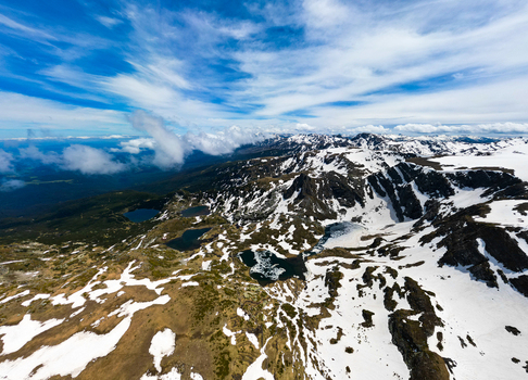 Aerial view of Seven Rila Lakes with snow capped mountain peaks glacial lakes and rocky terrain under a blue sky in Kyustendil Province Bulgaria. Aerial view of Seven Rila Lakes with snow capped mountain peaks glacial lakes and rocky terrain under a blue sky in Kyustendil Province Bulgaria.