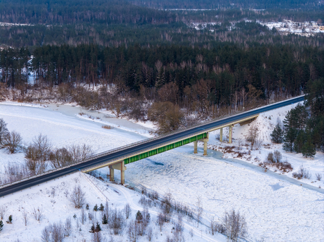 Aerial view of a bridge crossing a frozen river surrounded by snow covered banks and a dense evergreen forest Lithuania. Aerial view of a bridge crossing a frozen river surrounded by snow covered banks and a dense evergreen forest Lithuania.