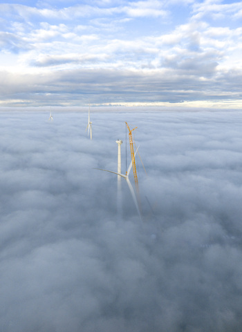 Aerial view of wind turbines and a yellow construction crane emerging from a thick layer of clouds under a blue sky Netherlands. Aerial view of wind turbines and a yellow construction crane emerging from a thick layer of clouds under a blue sky Netherlands.