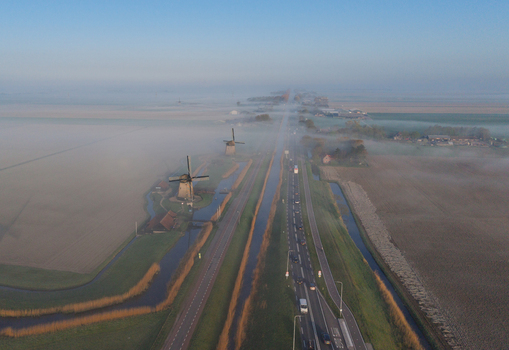Aerial view of traditional windmills standing beside a canal and a busy road shrouded in morning mist over flat polder landscapes Schermerhorn North Holland Netherlands. Aerial view of traditional windmills standing beside a canal and a busy road shrouded in morning mist over flat polder landscapes Schermerhorn North Holland Netherlands.