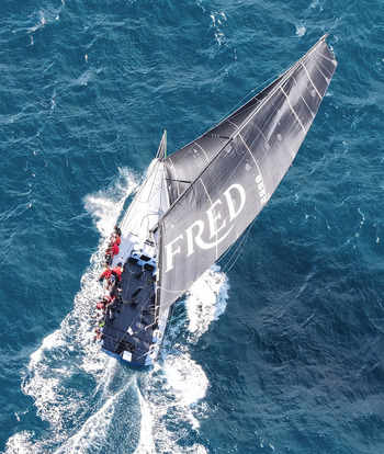 Sydney Harbour Area Australia 26 July 2025 Aerial view of a racing sailboat with a black sail marked FRED sailing through the blue waters of Sydney Harbour with crew.