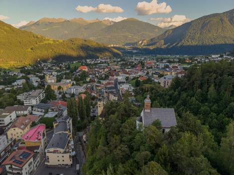 Aerial view of St. Laurentius Church nestled in the alpine town surrounded by lush forests and mountain peaks in Imst Tyrol Austria.
