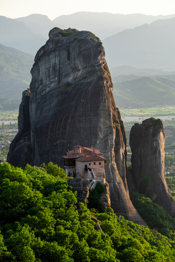 Aerial view of Meteora monastery perched on a massive rock formation surrounded by lush green trees and distant mountains in Trikala Greece. Aerial view of Meteora monastery perched on a massive rock formation surrounded by lush green trees and distant mountains in Trikala Greece.