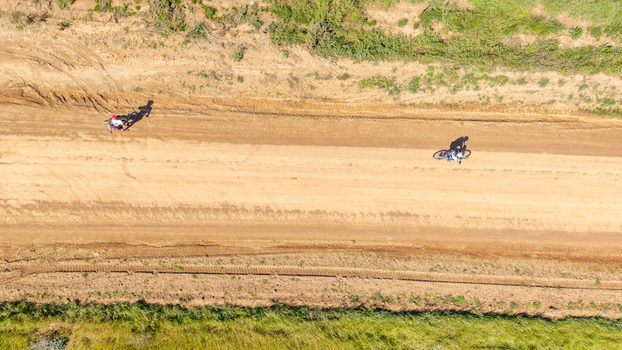 Aerial view of two cyclists riding mountain bikes along a dusty dirt road surrounded by green fields in the countryside in Greyton Western Cape South Africa.