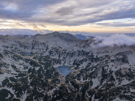 Aerial view of Pirin National Park featuring rugged mountain peaks glacial lakes and rocky terrain under a soft sunset sky in Blagoevgrad Province Bulgaria. Aerial view of Pirin National Park featuring rugged mountain peaks glacial lakes and rocky terrain under a soft sunset sky in Blagoevgrad Province Bulgaria.