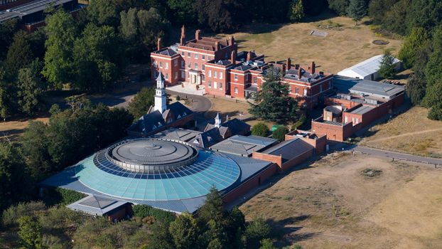 Aerial view of the Wellcome Genome Campus featuring a historic red brick building and a modern circular glass domed structure surrounded by lush parkland in Hinxton England United Kingdom. Aerial view of the Wellcome Genome Campus featuring a historic red brick building and a modern circular glass domed structure surrounded by lush parkland in Hinxton England United Kingdom.
