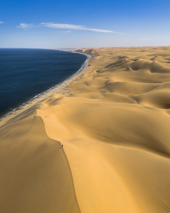 Aerial view of golden dunes meet the deep blue sea under a clear sky creating a stunning contrast of colors and textures Anichab Erongo Namibia. Aerial view of golden dunes meet the deep blue sea under a clear sky creating a stunning contrast of colors and textures Anichab Erongo Namibia.