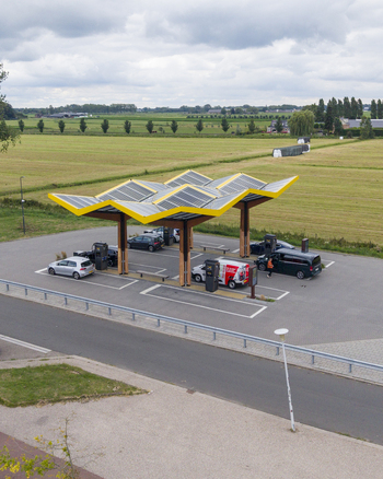 Aerial view of the Fastned Charging Station with its distinctive yellow solar roof surrounded by green fields and parked electric vehicles in Breukelen Utrecht Netherlands. Aerial view of the Fastned Charging Station with its distinctive yellow solar roof surrounded by green fields and parked electric vehicles in Breukelen Utrecht Netherlands.