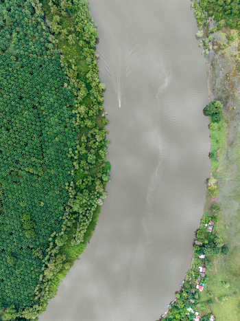 Aerial view of a small boat navigating a winding river flanked by dense tropical vegetation and small riverside houses in Costa Rica.