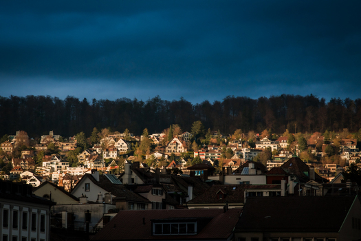 Zurich Switzerland 02 April 2023 View of buildings scattered across the landscape a tapestry of light and shadow playing upon their rooftops set against a backdrop of dark dense forest. Zurich Switzerland 02 April 2023 View of buildings scattered across the landscape a tapestry of light and shadow playing upon their rooftops set against a backdrop of dark dense forest.