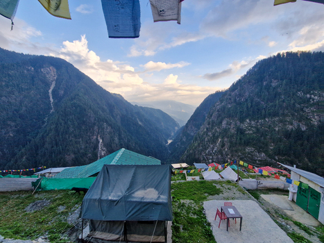 View of the mountainous landscape with camping tents colorful prayer flags and a table set in the foreground under a cloudy sky in Malana Himachal Pradesh India.