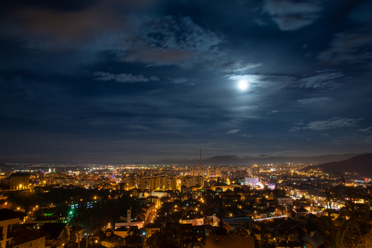 View of the illuminated cityscape of Brasov under a full moon with dark clouds at night in Brasov Judetul Brasov Romania. View of the illuminated cityscape of Brasov under a full moon with dark clouds at night in Brasov Judetul Brasov Romania.