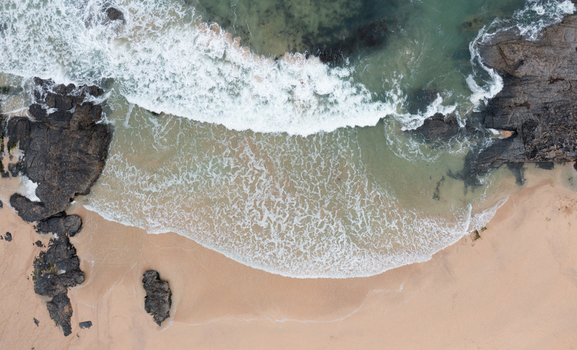Aerial view of waves crashing on the sandy shore of Harlyn Bay Beach with dark coastal rocks in Saint Merryn Cornwall United Kingdom.