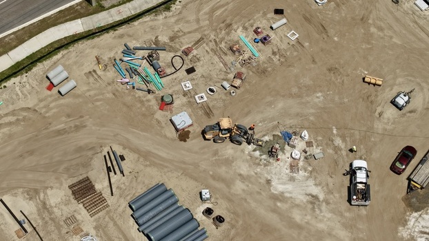 Aerial view of the construction site at Foundry Lane featuring heavy machinery large drainage pipes and workers on the sandy ground in World Golf Village Florida United States.