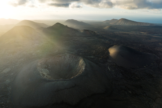 Aerial view of volcanic craters and rugged mountains under a dramatic sky with sunbeams in Lanzarote Canarias Spain. Aerial view of volcanic craters and rugged mountains under a dramatic sky with sunbeams in Lanzarote Canarias Spain.