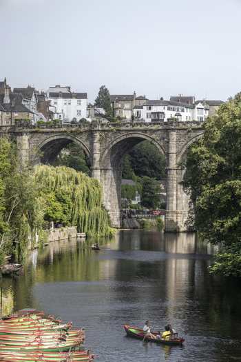 View of the historic Knaresborough Viaduct spanning the River Nidd with rowboats and people enjoying the water in Knaresborough England United Kingdom.