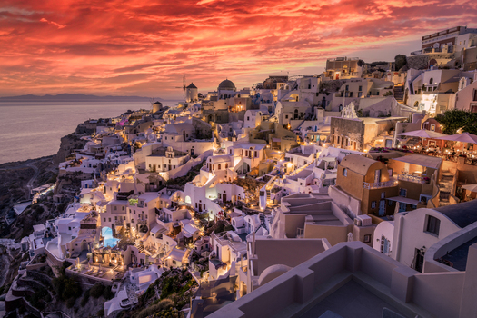 View of the iconic white buildings blue domes and windmills of Oia village perched on the cliffs overlooking the Aegean Sea during a vibrant sunset in Oia Greece.