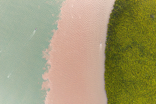 Aerial view of the confluence of two rivers with contrasting water colors dense mangrove forests along the bank and small boats navigating the waterway in Opobo Town Rivers Nigeria. Aerial view of the confluence of two rivers with contrasting water colors dense mangrove forests along the bank and small boats navigating the waterway in Opobo Town Rivers Nigeria.