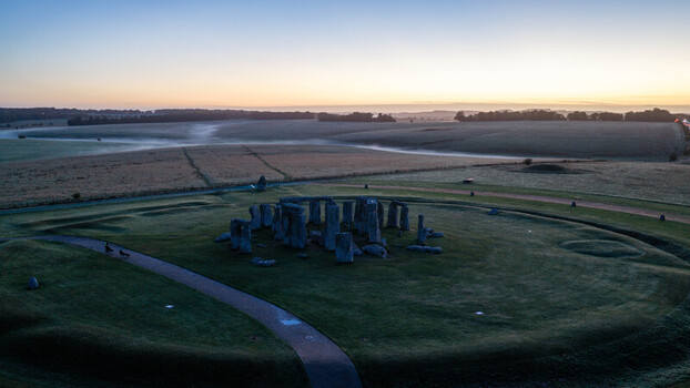 Aerial view of Stonehenge at sunrise with mist over the surrounding fields and ancient stone circle in Salisbury England United Kingdom. Aerial view of Stonehenge at sunrise with mist over the surrounding fields and ancient stone circle in Salisbury England United Kingdom.