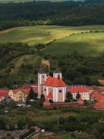 Aerial view of the Church of Saint Nicholas with its red roof and twin towers surrounded by village houses and rolling green hills in Sivice South Moravian Region Czechia.
