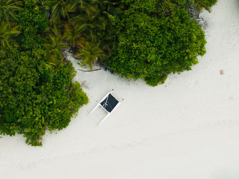 Aerial view of a lone white boat resting on the pristine white sands embraced by vibrant green foliage Vashafaru Island Thiladhummathi Atoll Maldives. Aerial view of a lone white boat resting on the pristine white sands embraced by vibrant green foliage Vashafaru Island Thiladhummathi Atoll Maldives.